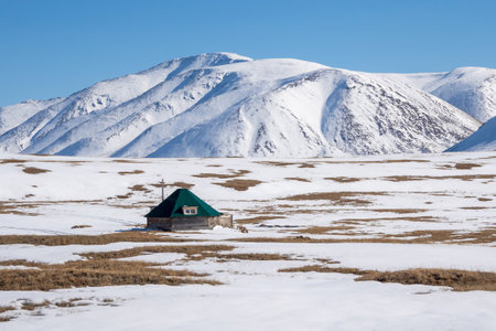 Snow covered mountains during winter season. Remote mountain cabin by a frozen meadow. Location in Altai region.の写真素材