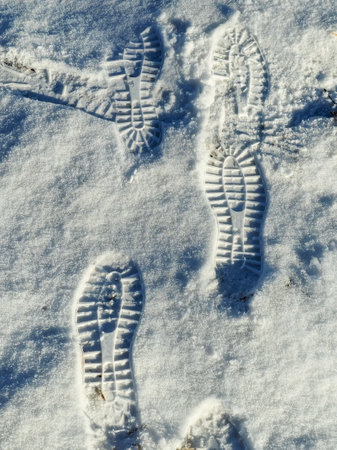 Foot prints mans boot in the snow. Sunny day in winter, vertical view.
