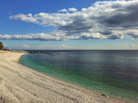 Pebble beach and blue sea with white clouds. Natural minimalistic seascape in sunny weather. Coast of the Crimean Peninsula.の写真素材