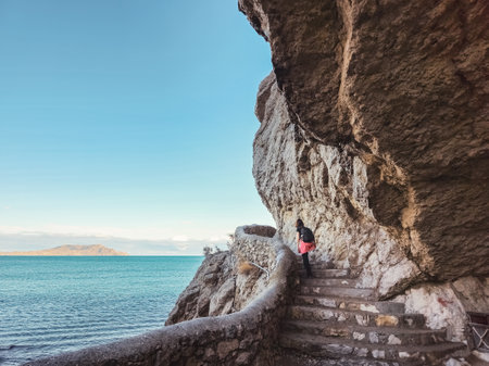 A stone trail along the edge of the cliff in the village of Novy Svet on the shore of Sudak-Liman Bay, Crimean Peninsula. Female tourist on a mountain trail view from the back.の写真素材