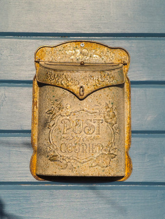 Picture of an antique golden letter box at a sunny blue wooden door, vertical view.