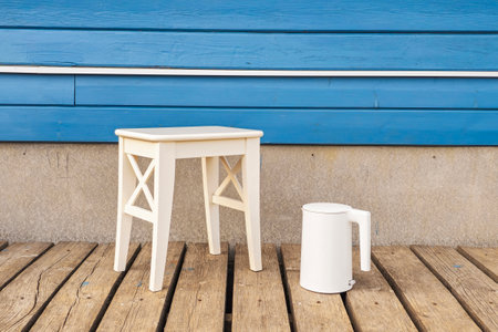 Electric white kettle and a white stool against a blue wooden home wall. Wooden flooring of a country house. Copy space. Minimalistic view.の写真素材