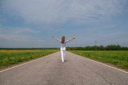 Happy slim woman running on country road in summer. Liberty, peace of mind concept. Back view.の写真素材