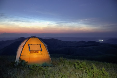 Camping at dusk. The night is drawing near, the stars are shining in the sky, and the light is on in...