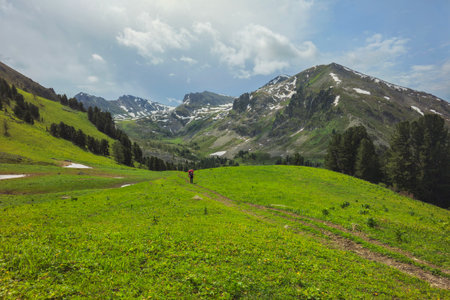 Mountain trekking is a challenging route. Solo hiking in the mountains. Silhouette of a lone hiker on a path through a valley in the highlands. The hiking path offers stunning views of the landscape.の写真素材