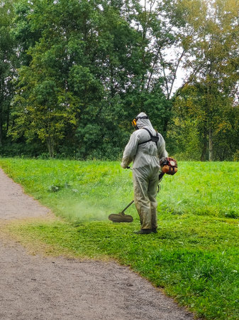 Unrecognizable man in uniform mows the lawn in city park. Maintenance cleaning of the park area. Vertical view.の写真素材