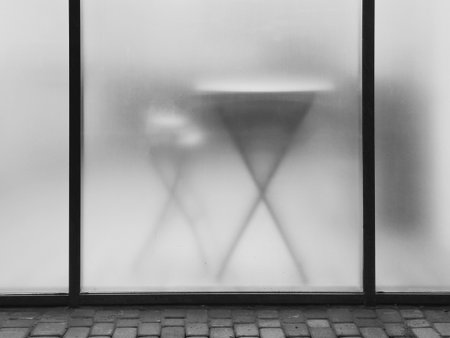 A blurred black and white transparent plastic glass with a table and chair behind it, used for the...
