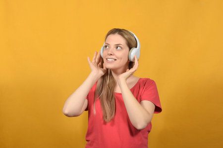 Portrait of young woman listening to music with headphones on yellow backgroundの写真素材