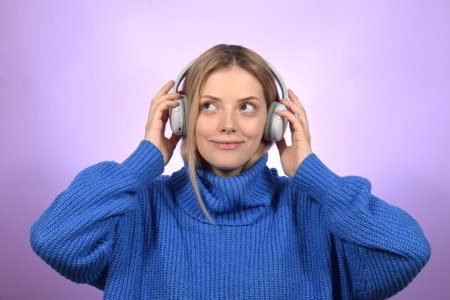 Young woman listening to music with headphones on purple background, closeup