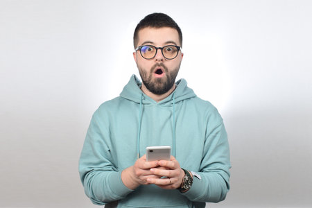 Portrait of a young man in a blue hoodie with glasses and a phone in his hands.
