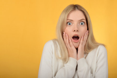 Surprised young woman on yellow background. Shocked girl looking at cameraの写真素材