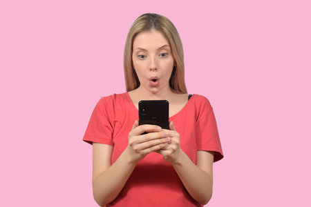 Young excited woman playing online game on mobile phone isolated over pink backgroundの写真素材