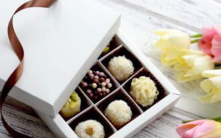 Box of assorted chocolate candies and tulips on white wooden background