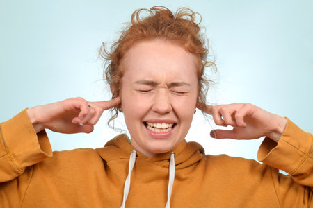Portrait of a red-haired girl closing her ears with fingers