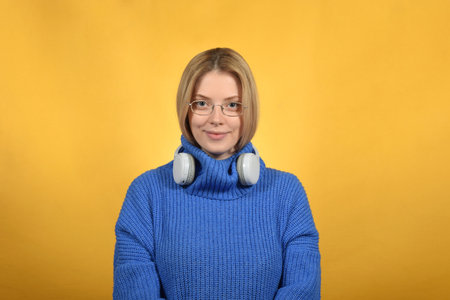 Young woman in a blue sweater on a yellow background in the studioの写真素材