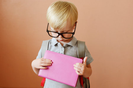 Cute little boy in eyeglasses holding a pink book.の写真素材