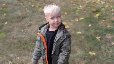 Little boy with blond hair in a green jacket on the background of autumn leaves