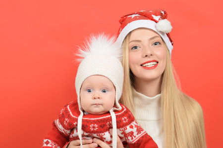 Happy mother and baby in Santa hats on red background. Christmas and New Year conceptの写真素材
