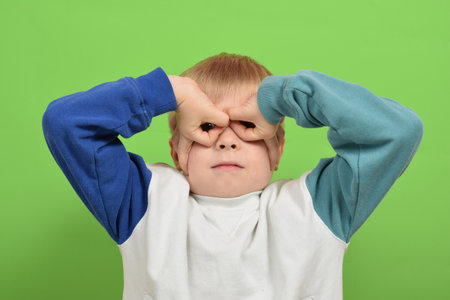 Portrait of a boy on a green background. The child looks through his fingers.の写真素材