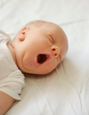 Portrait of a cute newborn baby lying on the bed and yawning