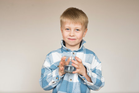 Portrait of a little boy with a glass of water on a gray backgroundの写真素材