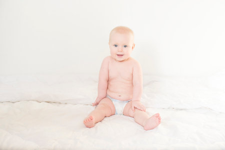 Cute baby boy sitting on bed and smiling at camera over white backgroundの写真素材