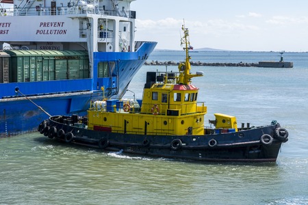 A yellow tugboat assisting a large cargo ship. Stock photo.の写真素材