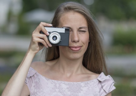 Beautiful woman is taking picture with old fashioned camera, outdoors.