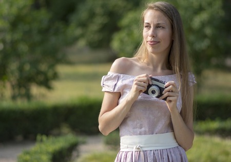 Beautiful woman is holding old fashioned camera in hand, outdoors.の写真素材