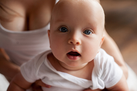 Portrait of small baby. Kid sitting and looking with surprise. Mother holding baby.の写真素材