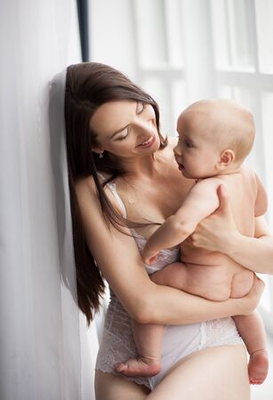 Young mother holds her naked baby on hands. They are sitting and smiling.の写真素材