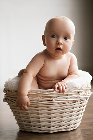 Little baby sits in a wicker basket. He looks very surprised.の写真素材