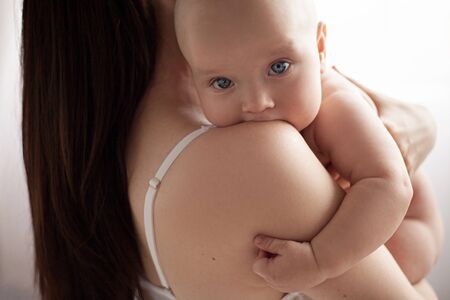 Baby on hands his mother. He hugs her and looks out over her shoulder.の写真素材