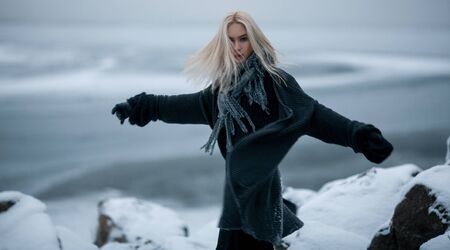 Girl in snow on winter background. She stands among rocks and wind blowing her hair. の写真素材