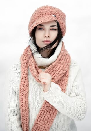 Portrait of girl in sweater, hat and scarf. Scarf wrapped around her neck. Against white background.の写真素材
