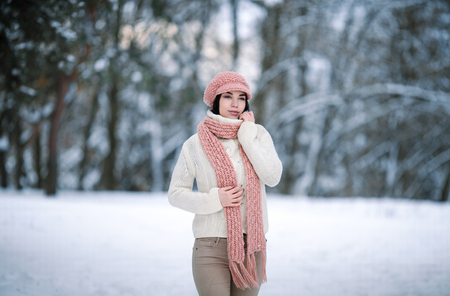 Girl in sweater scarf and hat in winter forest. She wrapped herself in sweater and scarf.の写真素材