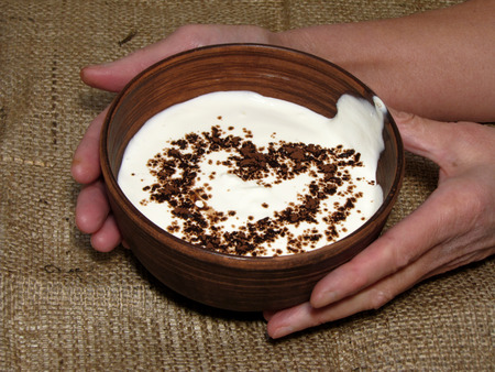 Romantic breakfast with painted heart on Valentine's Day on jute background. Sour cream served in handmade old pottery. Heart is drawn from chocolate. Bowl holding with hands.                               の写真素材