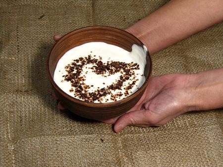 Romantic breakfast with painted heart on Valentine's Day on jute background. Sour cream served in handmade old pottery. Heart is drawn from chocolate. Bowl holding with hands.                               の写真素材