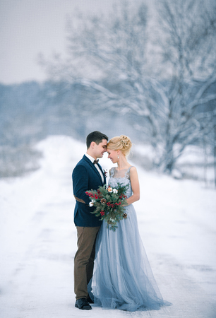 Bride and groom among snowy landscape. Bride and groom are standing and hugging.  Winter wedding outdoors.の写真素材