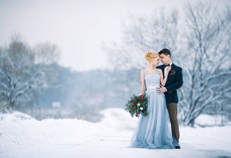 Bride and groom among snowy landscape. Bride and groom are standing and hugging.  Winter wedding outdoors. Copy space.の写真素材