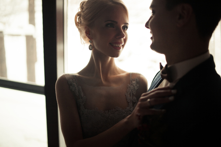 Portrait of smiling bride and groom on window background. Bride is smiling and tenderly looks at groom.の写真素材