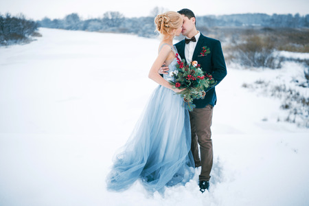 Bride and groom are kissing among snowy landscape. Bride and groom are standing, kissing and hugging.  Winter wedding outdoors.の写真素材