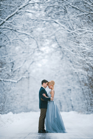 Bride and groom among snowy road in forest. They are standing and hugging.  Winter wedding outdoors.の写真素材