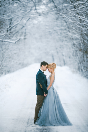 Bride and groom are holding hands among snowy road in forest. They are standing.  Winter wedding outdoors.の写真素材