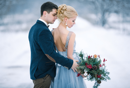 Bride and groom among snowy landscape. Bride and groom are standing and hugging.  View from back. Winter wedding outdoors.の写真素材