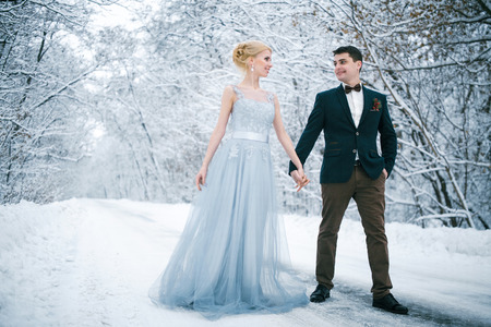 Bride and groom are holding hands among snowy road in forest. They are standing.  Winter wedding outdoors.の写真素材