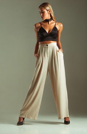 Suntanned girl in bra-top, slacks and high heels on gray background. She is standing.の写真素材