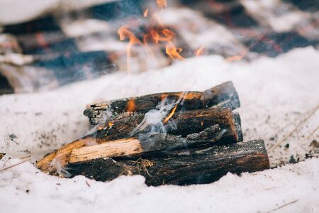 Burning firewood in campfire for winter picnic. Plaid is seen in snow background.の写真素材