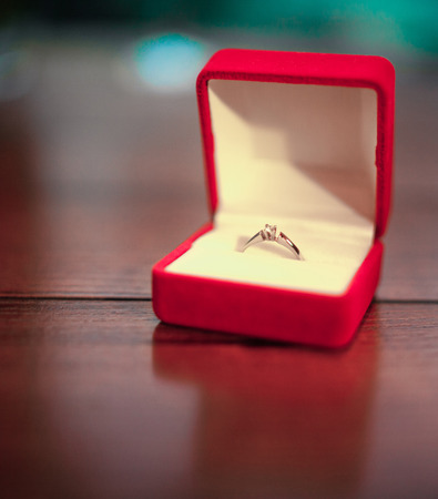 Opened red jewelry case with engagement ring on table. Gold ring with diamond. Close-up.の写真素材