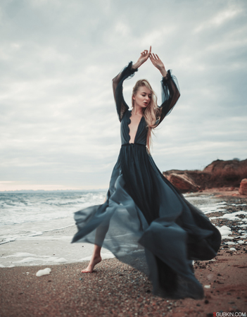 Young woman in long transparent black dress among beach and sea. Wind blows hem of her dress.の写真素材